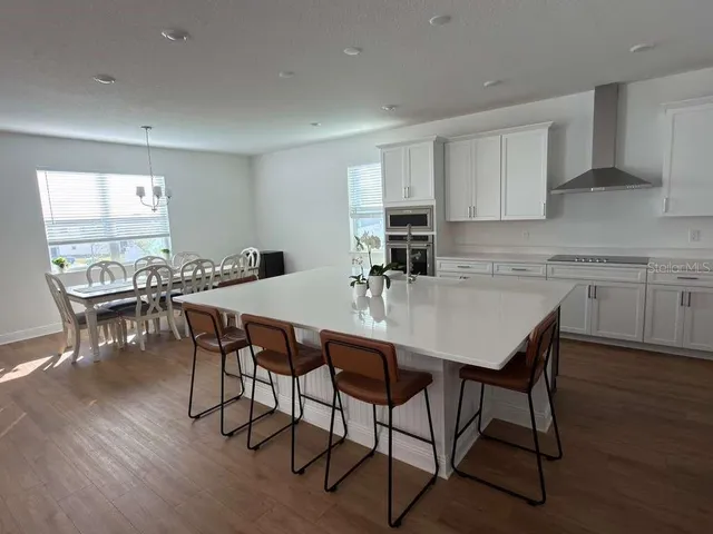 a kitchen with stainless steel appliances granite countertop a dining table chairs refrigerator and sink