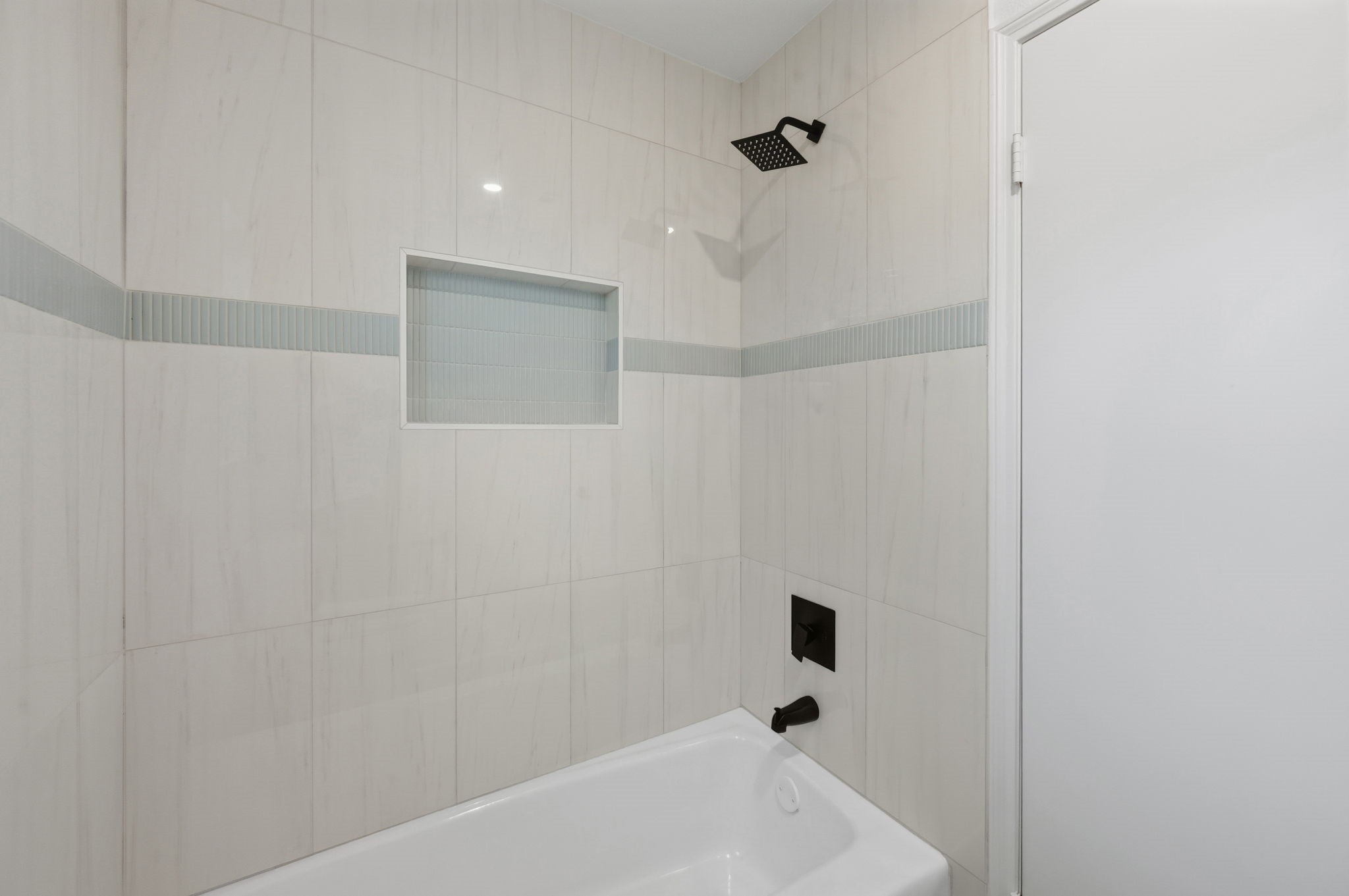 210 Ridgemont Drive Alvin, TX 77511 - Photo 18 of 27 This bathroom features a sleek, modern design with light tiled walls, a built-in shelf, and matte black fixtures. The tub and shower area is both stylish and functional.