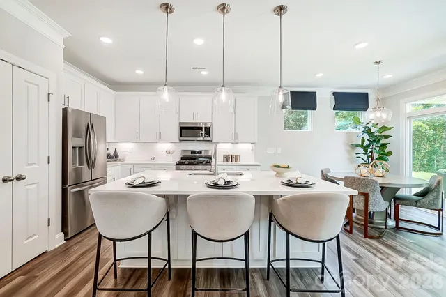 a kitchen with stainless steel appliances kitchen island granite countertop a dining table chairs refrigerator and sink