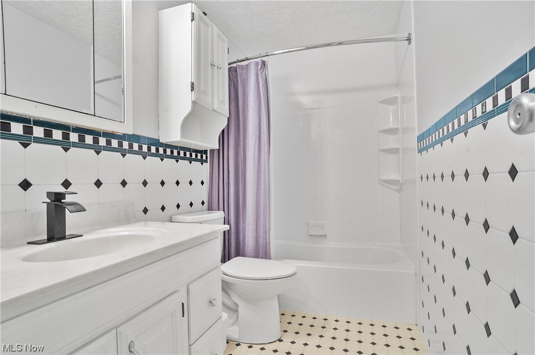 4252 Hile Road Stow, OH 44224 - Photo 14 of 31 Full bathroom with vanity, a textured ceiling, light tile floors, mirror, tile walls, backsplash, and shower / bath combo