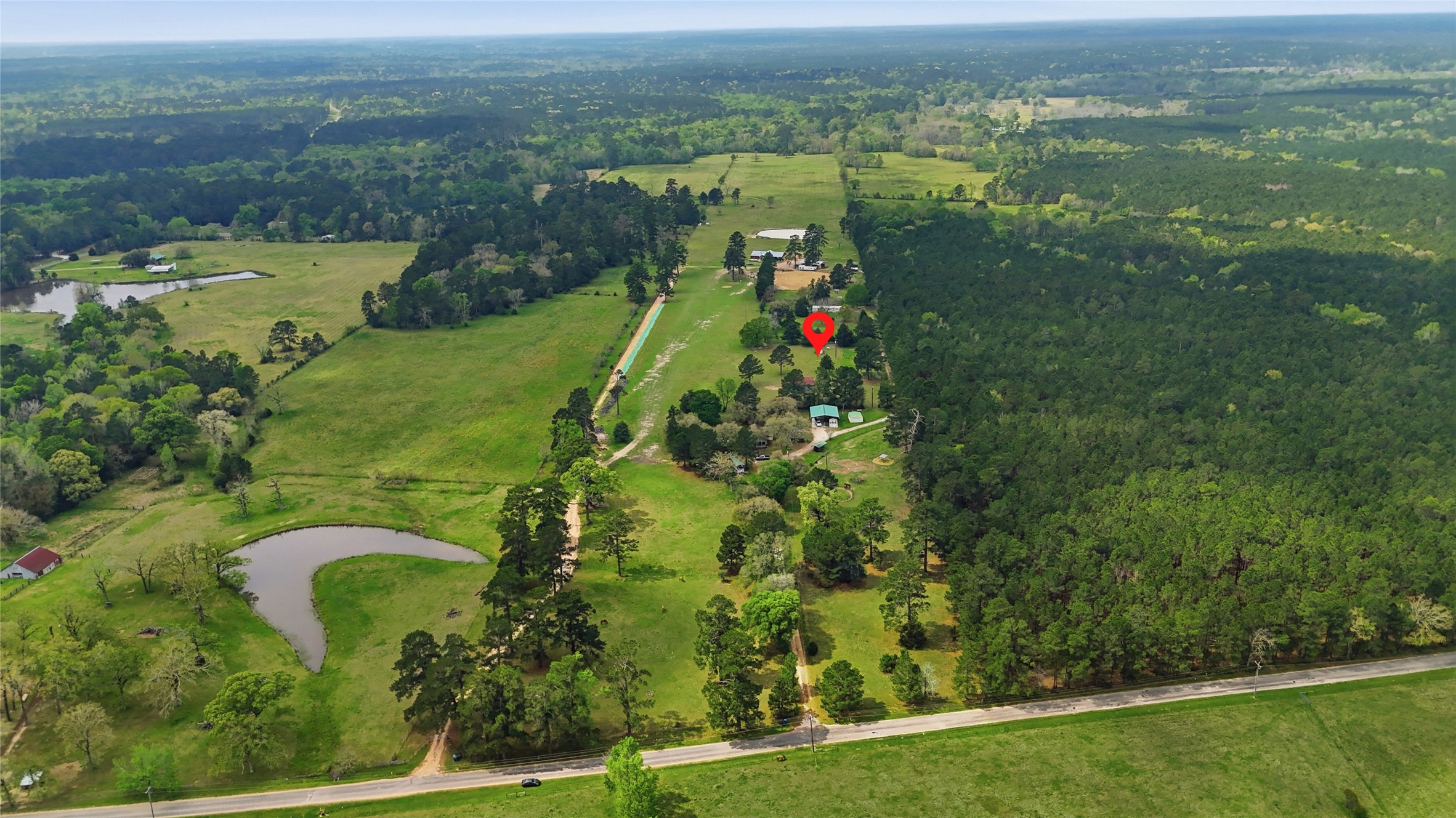 872 Four Notch Road Huntsville, TX 77340 - Photo 38 of 42 Expansive rural property featuring lush greenery, a serene pond, and a long, tree-lined driveway leading to a secluded home, surrounded by natural beauty.