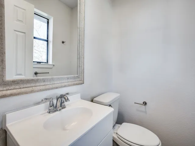 a bathroom with a toilet a sink a mirror and a window