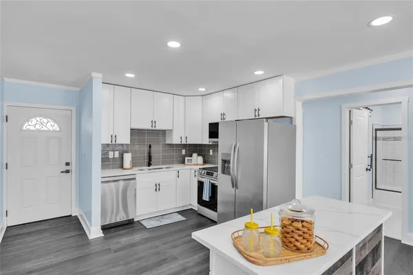 a kitchen with stainless steel appliances kitchen island granite countertop a refrigerator a sink a stove and white cabinets with wooden floor