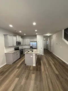 a large kitchen with kitchen island a stove a sink a refrigerator and white cabinets with wooden floor