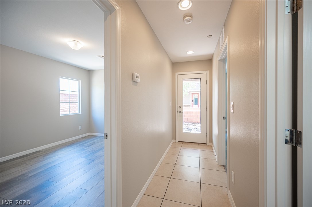 9916 Sable Point Street Las Vegas, NV 89178 - Photo 15 of 73 A well-lit interior hallway connects a room with wood-like flooring to an outdoor area through a glass-paneled door.