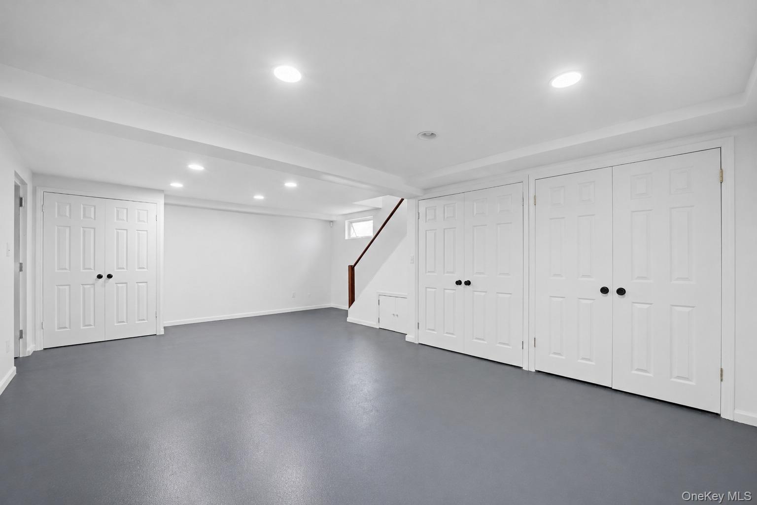 144 Bell Road Scarsdale, NY 10583 - Photo 33 of 49 Spacious basement recreation room featuring gray flooring, recessed lighting, multiple paneled closet doors with black hardware, and a staircase with a wood handrail