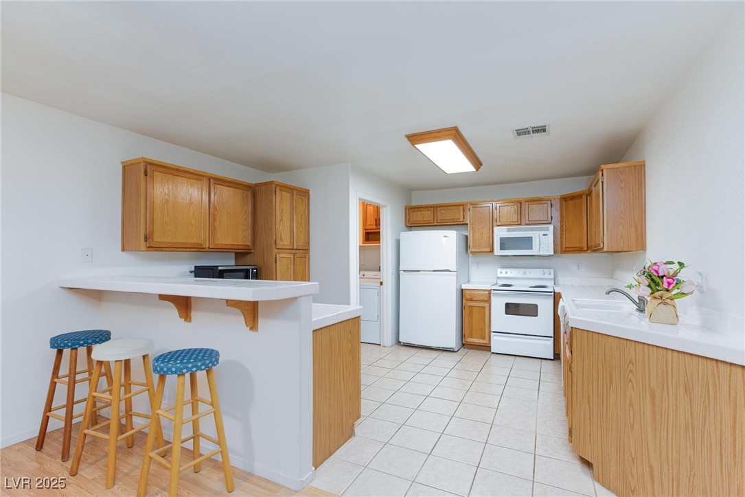3673 Ian Thomas Street, Unit 102 Las Vegas, NV 89129 - Photo 3 of 15 Kitchen with a kitchen breakfast bar, white appliances, a peninsula, light tile patterned floors, and tile countertops
