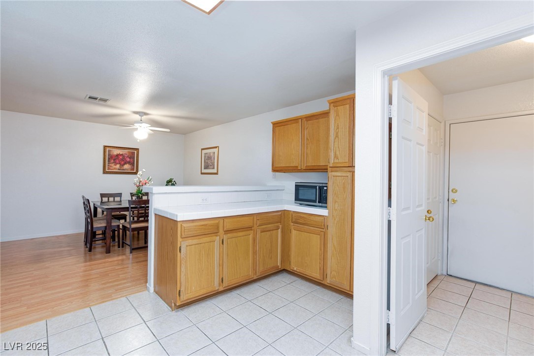 3673 Ian Thomas Street, Unit 102 Las Vegas, NV 89129 - Photo 4 of 15 Kitchen with a peninsula, light tile patterned floors, light countertops, a ceiling fan, and brown cabinets