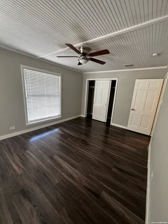 a view of an empty room with wooden floor and a ceiling fan