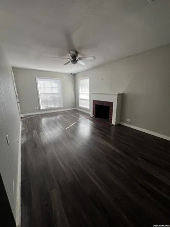 an empty room with wooden floor fireplace and windows