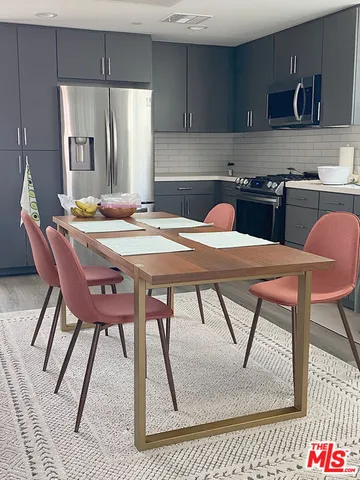 a kitchen with stainless steel appliances kitchen island granite countertop a dining table chairs and a refrigerator