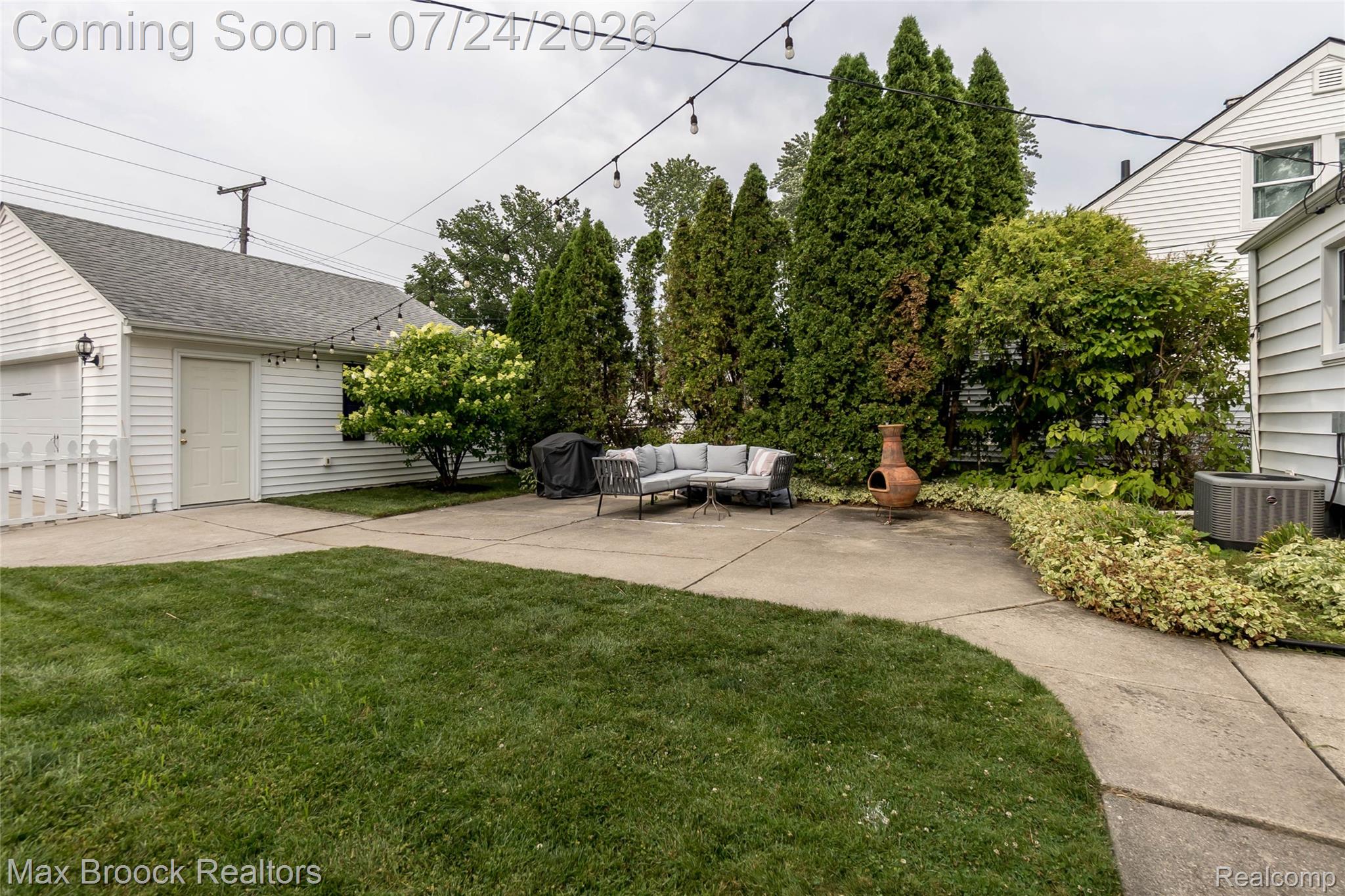 1090 Cambridge Road Berkley, MI 48072 - Photo 34 of 43 Expansive backyard featuring a concrete patio, a detached garage with a white picket fence, mature trees, and a well-maintained lawn