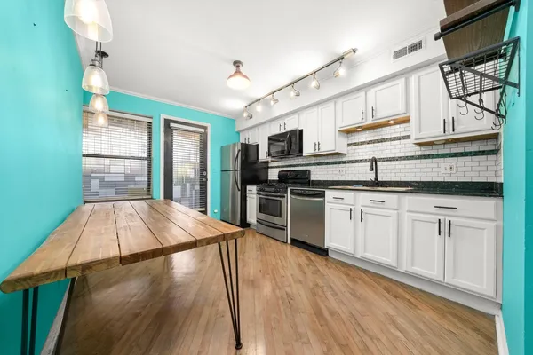 a kitchen with stainless steel appliances granite countertop a refrigerator a stove a sink dishwasher and white cabinets with wooden floor