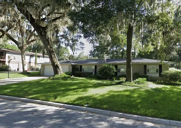 a backyard of a house with table and chairs plants and large tree