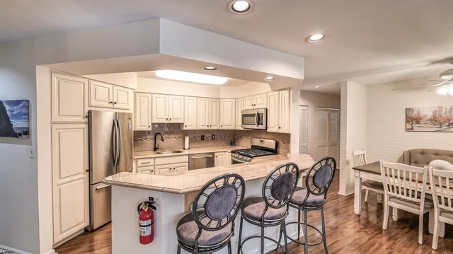 a kitchen with stainless steel appliances a refrigerator a stove a dining table and chairs with wooden floor