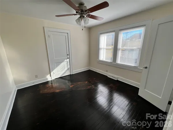 an empty room with wooden floor fan and windows