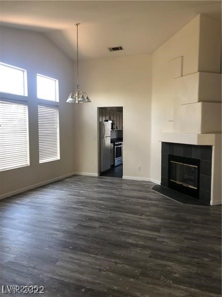 838 Rusty Anchor Way Henderson, NV 89002 - Photo 3 of 18 Unfurnished living room featuring a chandelier, dark wood-type flooring, a tiled fireplace, and high vaulted ceiling