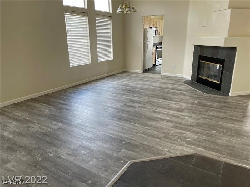 838 Rusty Anchor Way Henderson, NV 89002 - Photo 4 of 18 Unfurnished living room featuring a tiled fireplace, a chandelier, and dark wood-style flooring