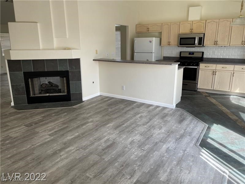 838 Rusty Anchor Way Henderson, NV 89002 - Photo 18 of 18 Kitchen featuring dark countertops, appliances with stainless steel finishes, decorative backsplash, open floor plan, and a tiled fireplace