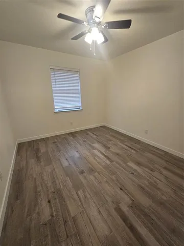 a view of an empty room with wooden floor and a fan