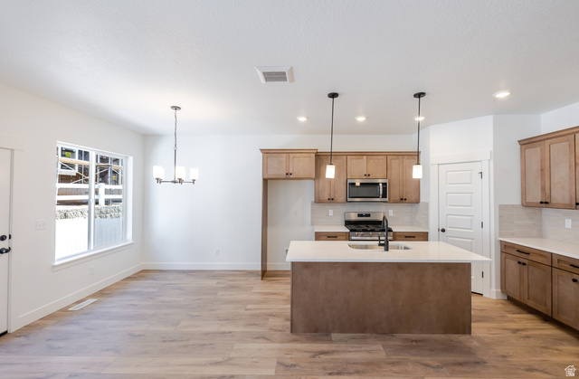4809 Olive Avenue, Unit 417 Mapleton, UT 84664 - Photo 3 of 18 Kitchen featuring stainless steel appliances, light wood-style floors, light stone counters, an island with sink, and hanging lights