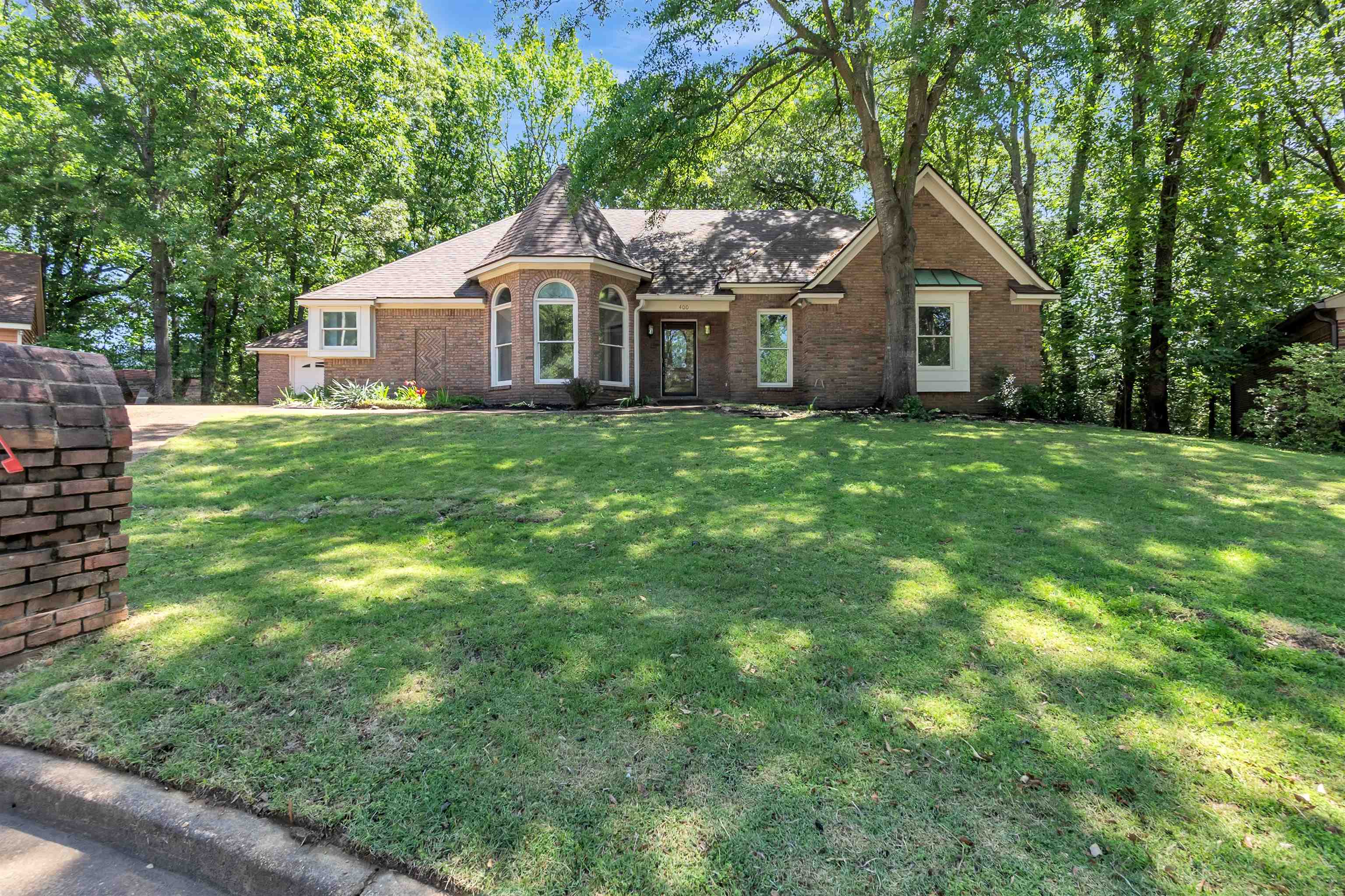400 Reksten Cove Memphis, TN 38018 - Photo 1 of 26 Brick exterior home with a turret architectural feature, arched windows, an integrated garage, and a lush green lawn surrounded by mature trees