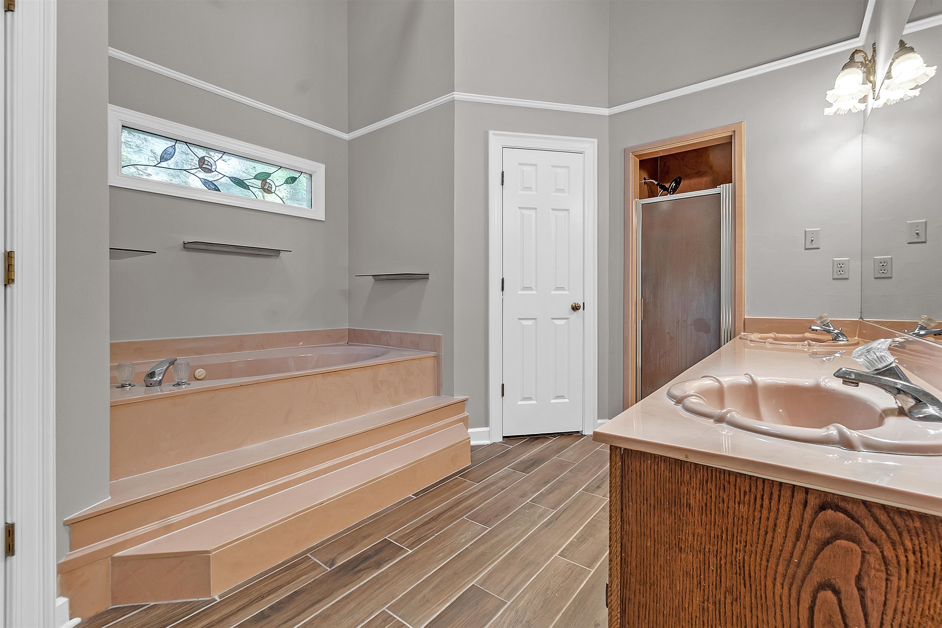 400 Reksten Cove Memphis, TN 38018 - Photo 18 of 26 Soaking tub with stepped surround, wood-finish flooring, stained-glass transom window, and a dual vanity with integrated sinks