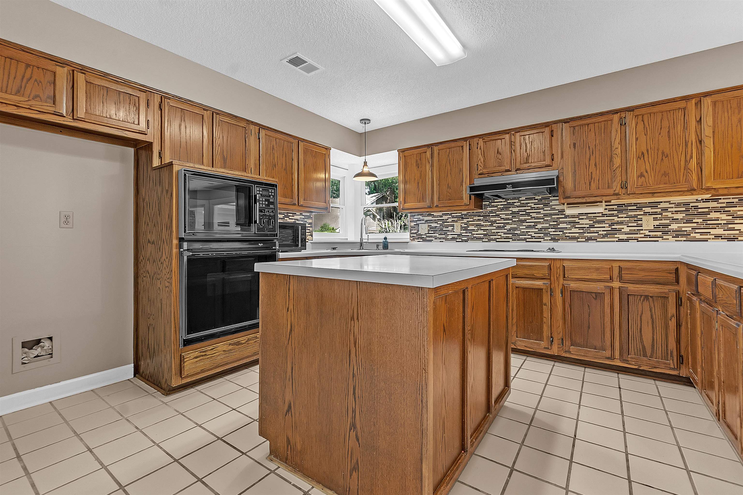 400 Reksten Cove Memphis, TN 38018 - Photo 8 of 26 Kitchen featuring wood-finish cabinetry, light-toned countertops, a central island, mosaic tile backsplash, and a built-in oven with microwave