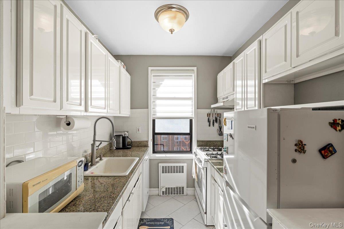 110-45 71st Road, Unit 6D Queens, NY 11375 - Photo 6 of 20 Kitchen with white cabinetry, white appliances, light tile patterned flooring, under cabinet range hood, and radiator heating unit