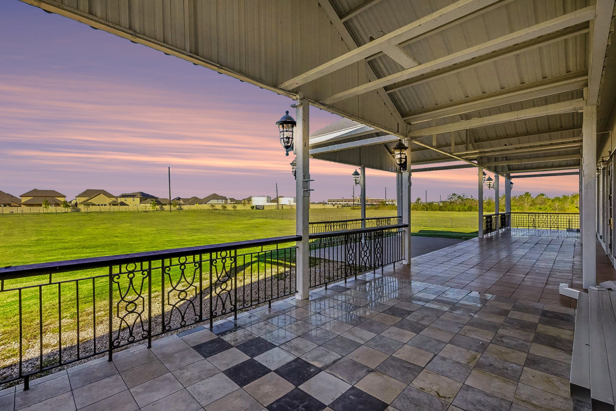 1200 Davenport Parkway Rosharon, TX 77583 - Photo 38 of 49 Charming front port-cochere-style porch elegantly tiled with checkerboard stone and terra-cotta flooring, beautifully accented by wrought iron railings and lantern lighting—perfectly framing tranquil sunset
and daytime views of the expansive property.
