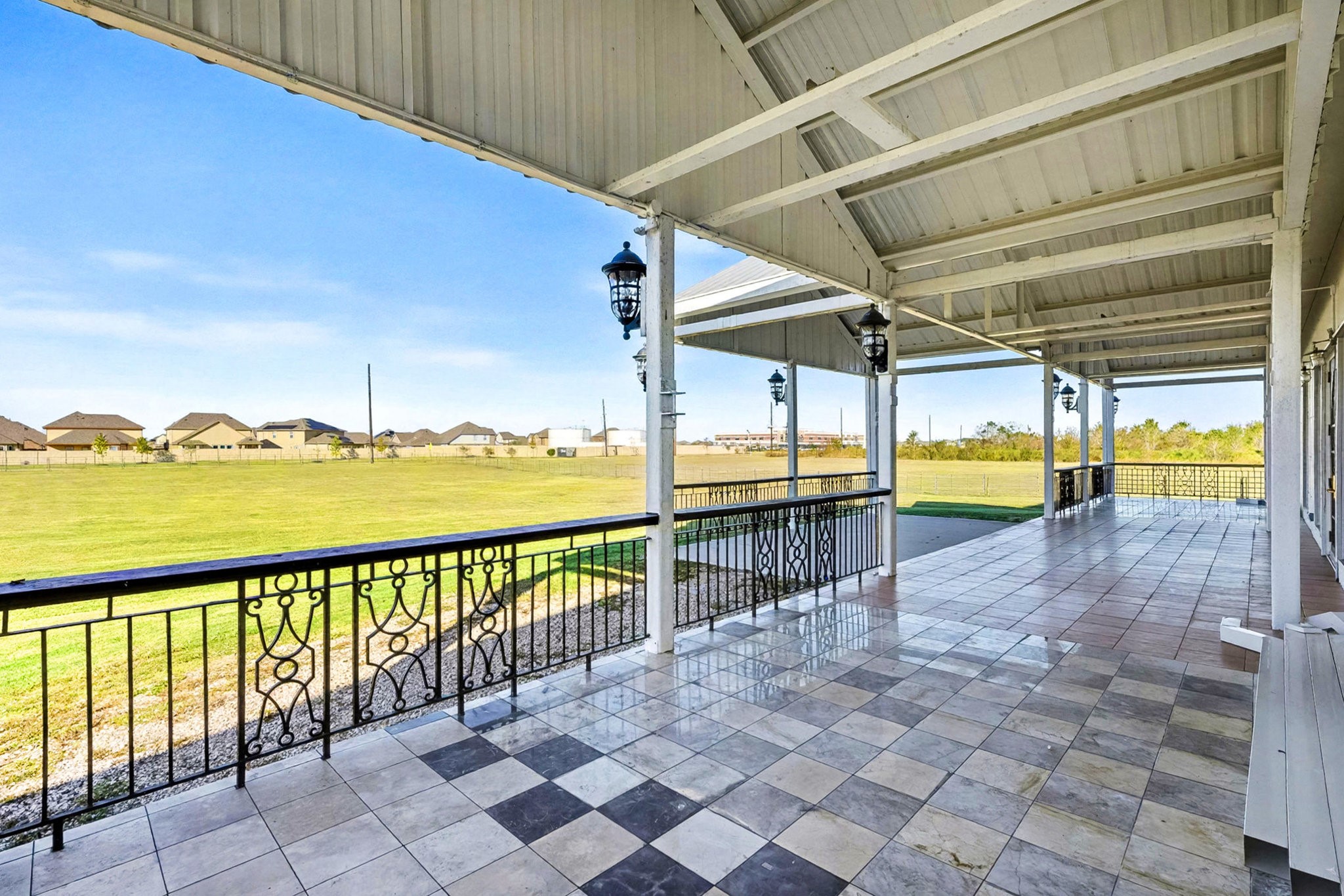 1200 Davenport Parkway Rosharon, TX 77583 - Photo 39 of 49 Charming front port-cochere-style porch elegantly tiled with terra-cotta checkered flooring, beautifully
accented by wrought iron railings and lantern lighting—perfectly framing tranquil sunset
and daytime views of the expansive property.