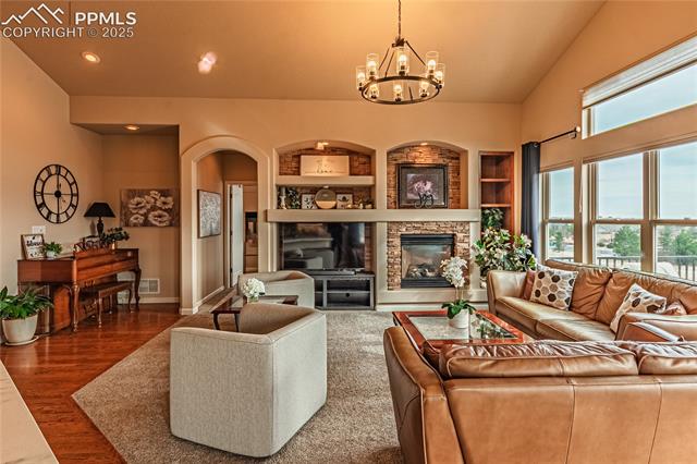 13812 Windy Oaks Road Colorado Springs, CO 80921 - Photo 17 of 50 Living room with baseboards, wood finished floors, built in features, arched walkways, and a notable chandelier