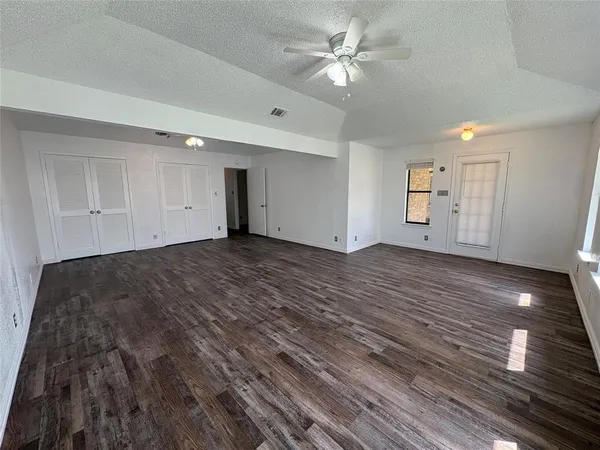 a view of an empty room with wooden floor and a ceiling fan