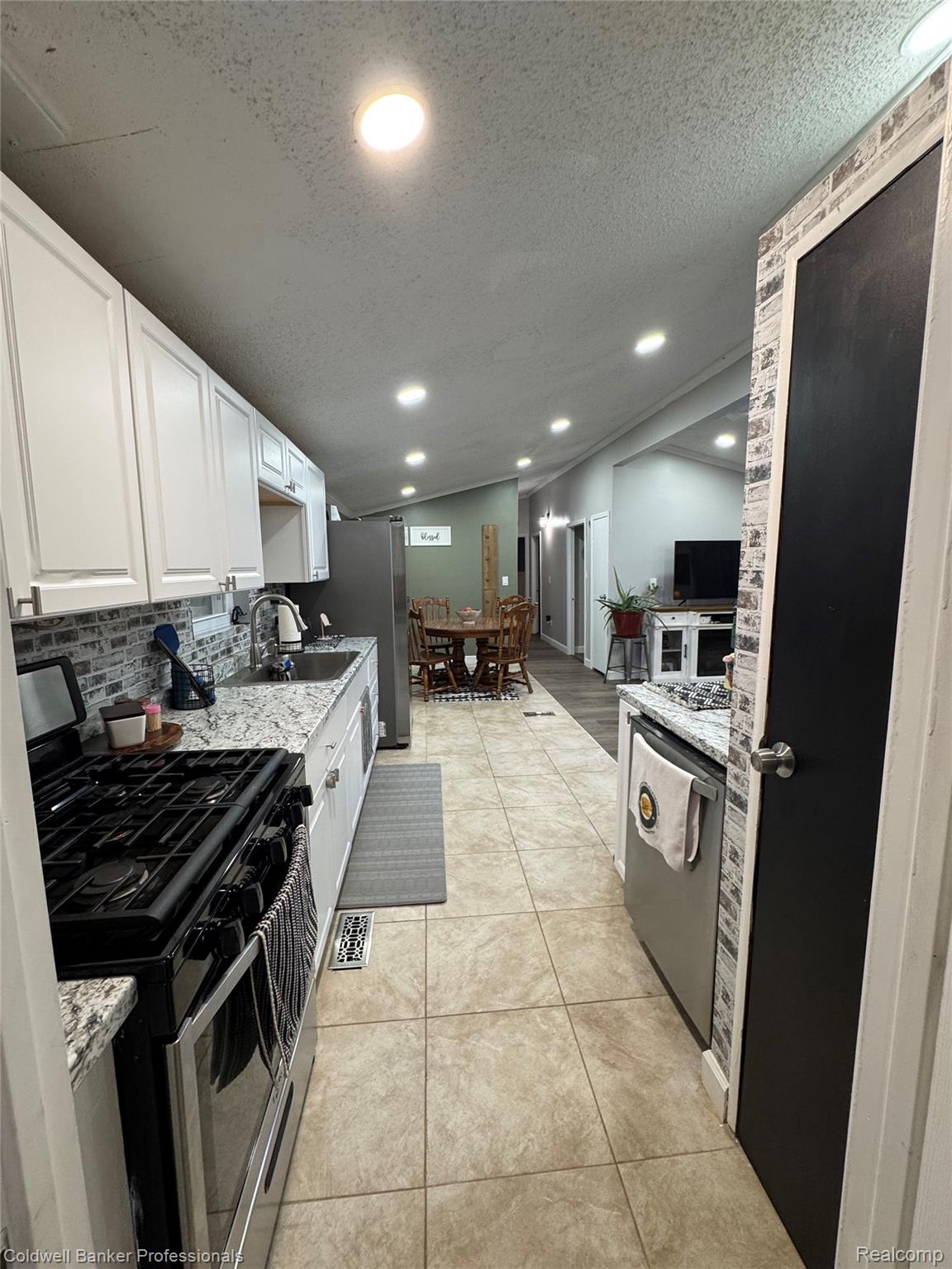 5323 English Road Clifford, MI 48727 - Photo 22 of 46 Kitchen featuring white cabinetry, a black range, stainless steel appliances, a tile backsplash, and light-toned tile flooring