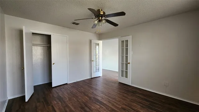 a view of an empty room with wooden floor and a ceiling fan