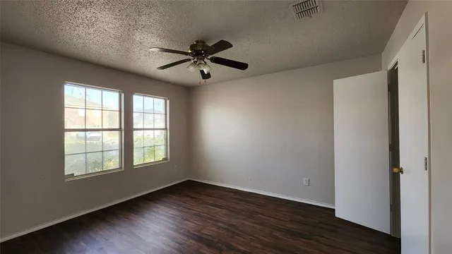 an empty room with wooden floor fan and windows
