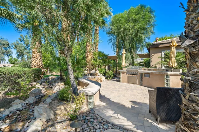 a view of a patio with couches table and chairs under an umbrella with large trees