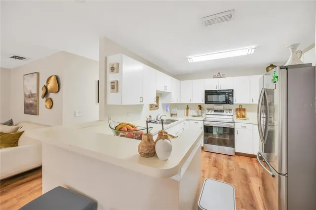 a white kitchen with stainless steel appliances a stove a sink a refrigerator white cabinets and wooden floor