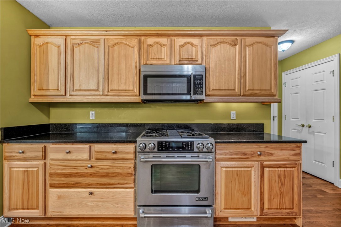 800 Bell Road Chagrin Falls, OH 44022 - Photo 11 of 35 Kitchen featuring appliances with stainless steel finishes, a textured ceiling, wood finished floors, light brown cabinetry, and dark stone countertops