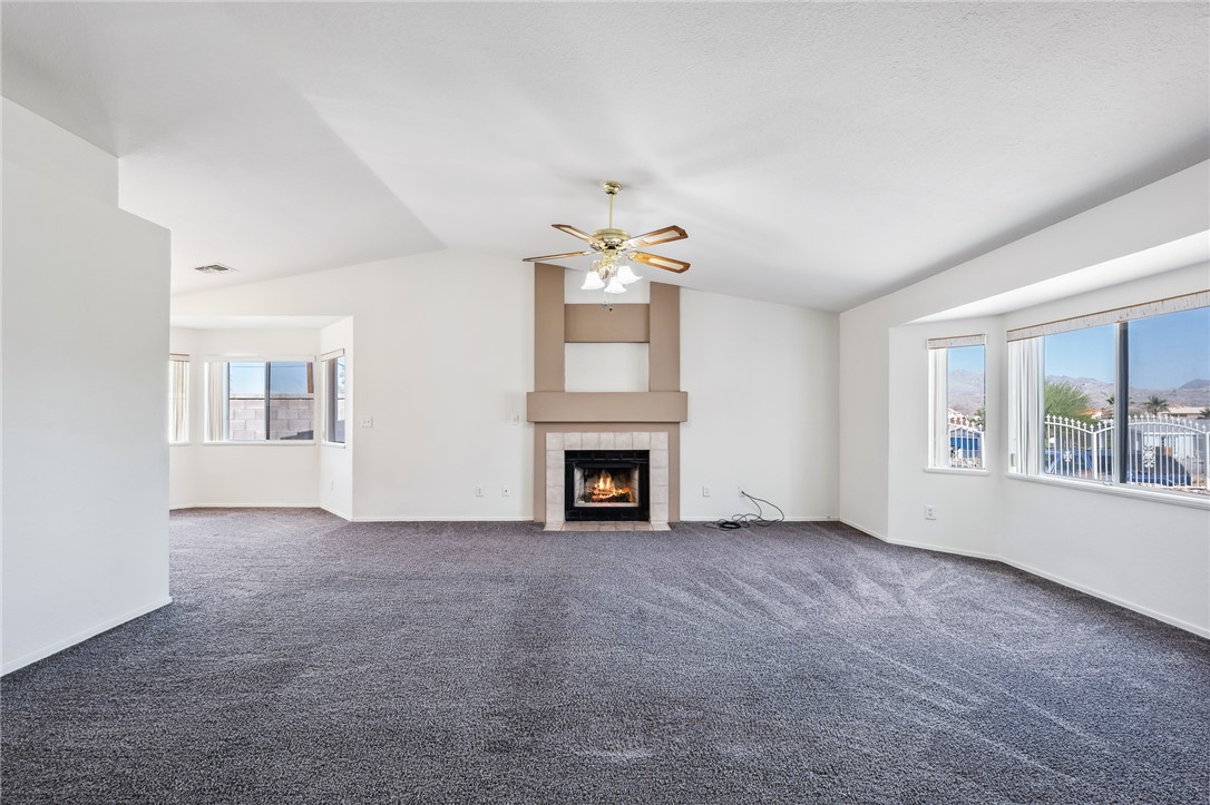 2524 South Ridge Avenue Bullhead City, AZ 86429 - Photo 12 of 64 Unfurnished living room featuring vaulted ceiling, a ceiling fan, plenty of natural light, carpet flooring, and a fireplace