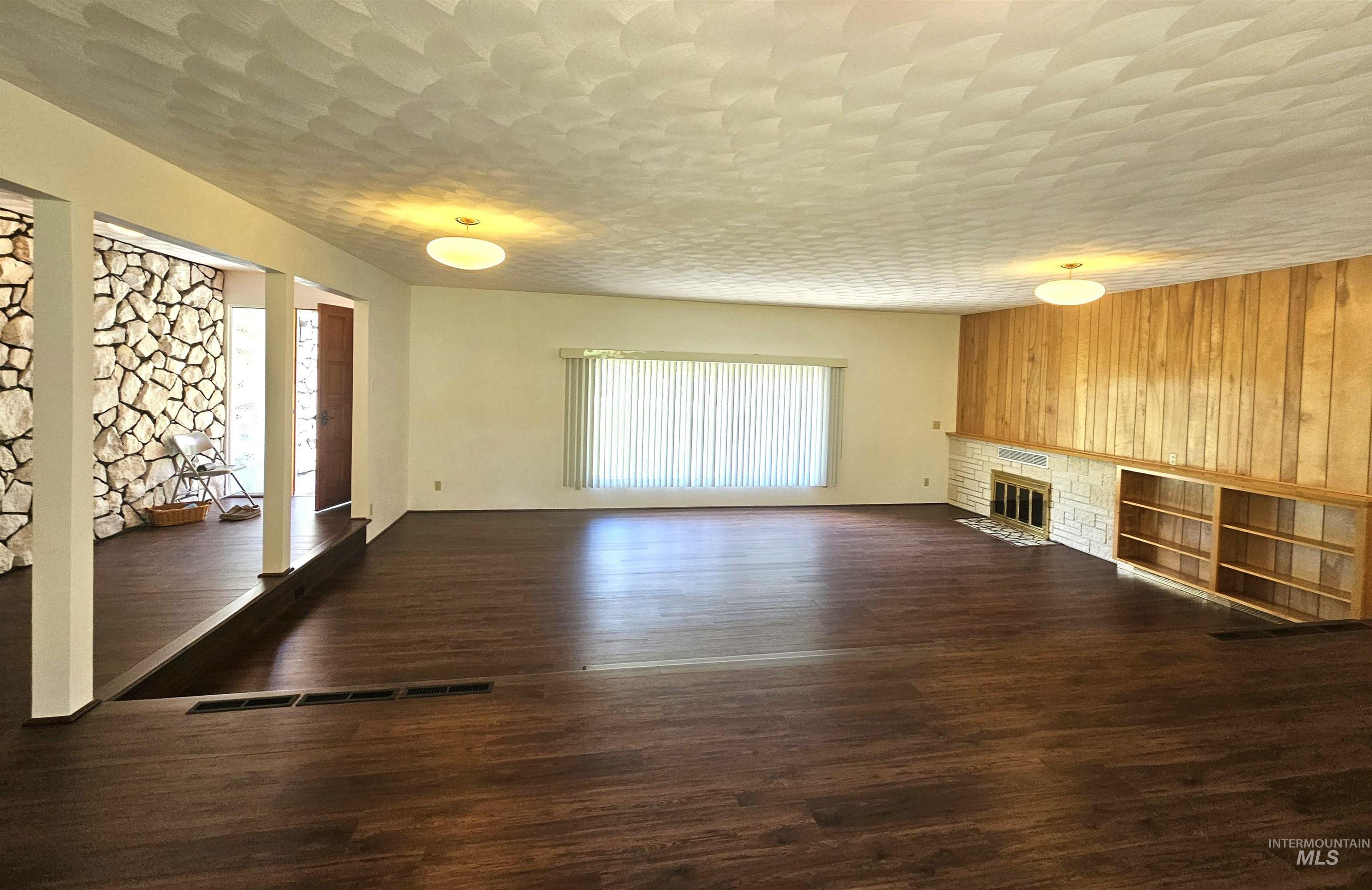 29865 Mission Creek Road Culdesac, ID 83524 - Photo 6 of 43 Spacious living area featuring wood-finish flooring, a stone fireplace with built-in shelving, wood paneled accent wall, and a textured ceiling