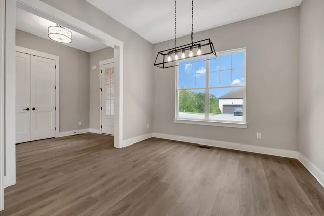 an empty room with wooden floor chandelier and windows