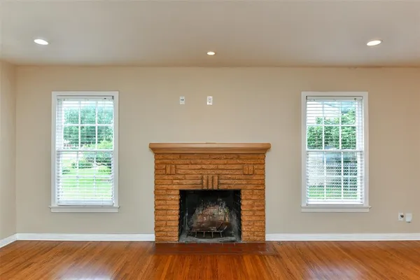 an empty room with wooden floor fireplace and windows