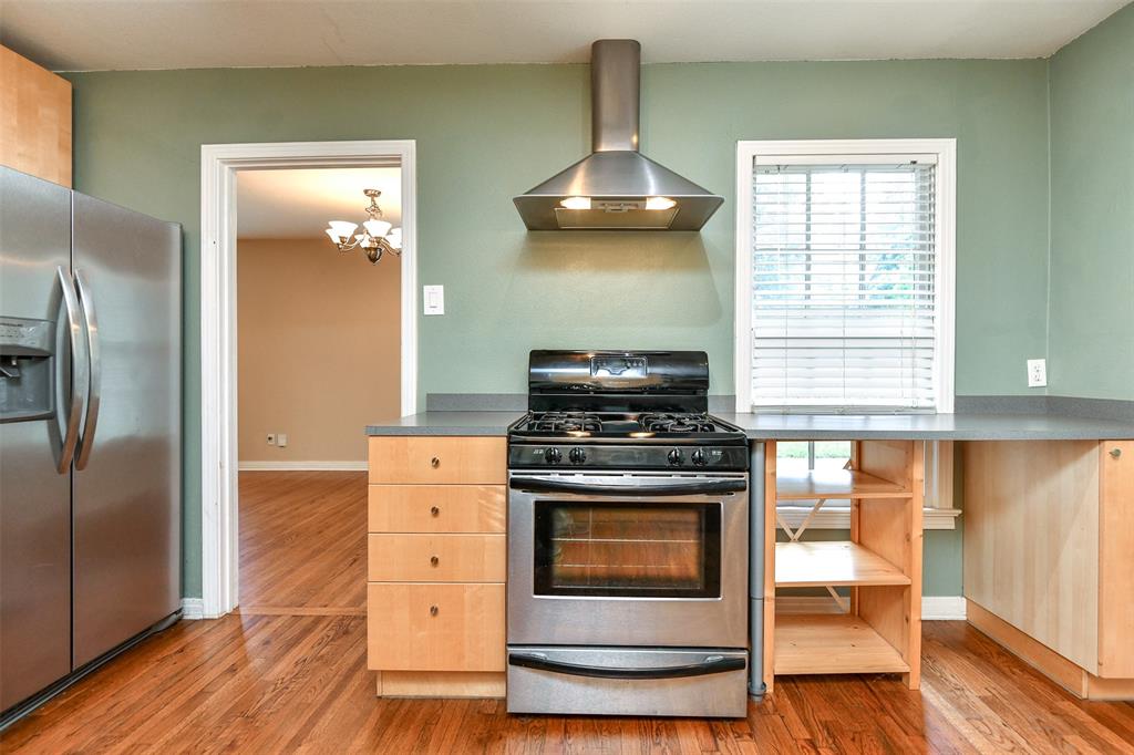 3516 Rashti Court Fort Worth, TX 76109 - Photo 8 of 24 Kitchen featuring appliances with stainless steel finishes, light brown cabinetry, wall chimney range hood, a chandelier, and hardwood / wood-style floors