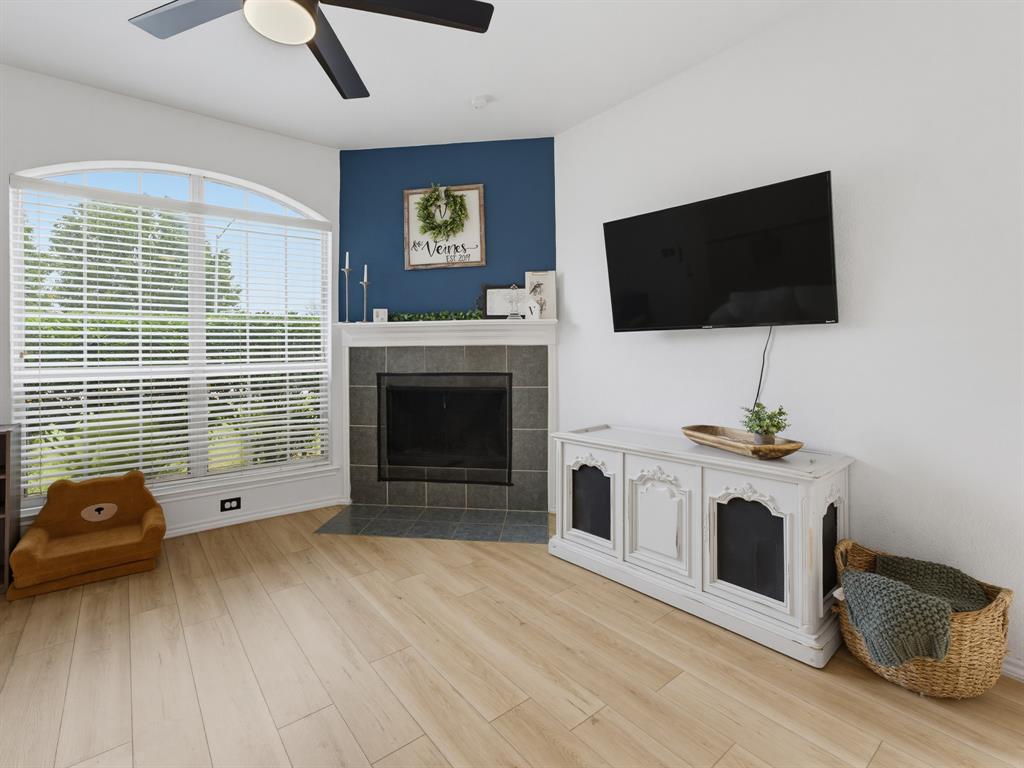 600 Stirling Road Rhome, TX 76078 - Photo 8 of 38 Living area with wood-finish flooring, a ceiling fan with integrated lighting, and a corner fireplace featuring a white mantle and dark tile surround