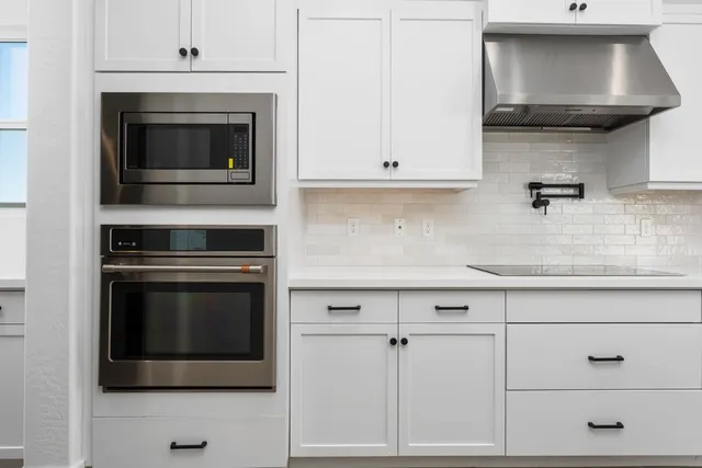 a large white kitchen with kitchen island a sink a center island stainless steel appliances and a window
