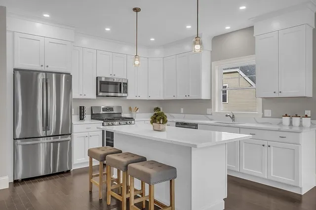 a kitchen with stainless steel appliances granite countertop a refrigerator a sink dishwasher a stove and white cabinets with wooden floors