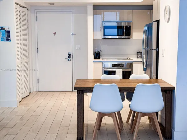 a kitchen with stainless steel appliances a dining table chairs a refrigerator and cabinets