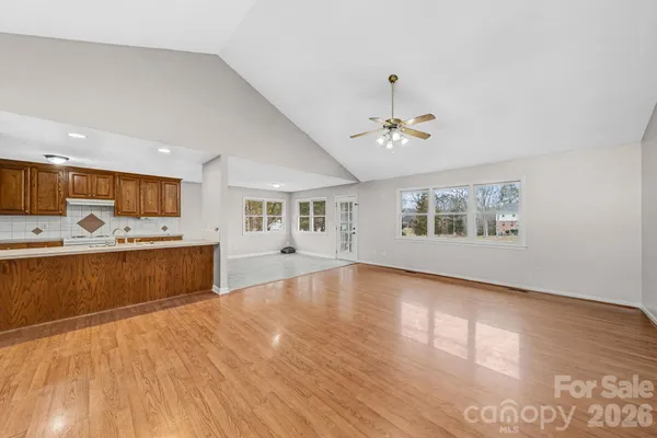 an empty room with wooden floor chandelier fan and windows