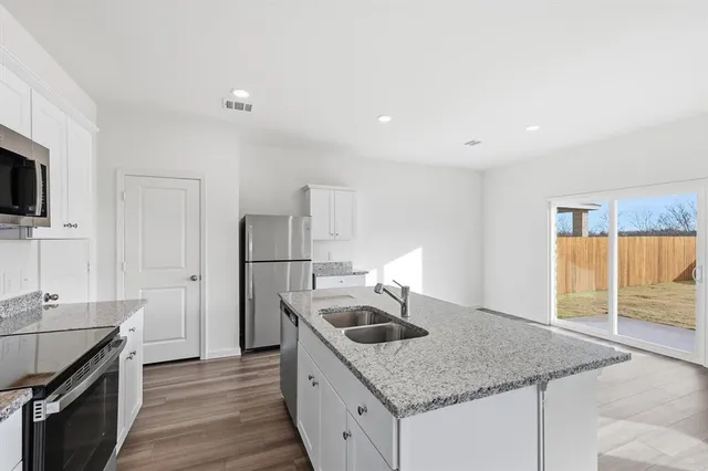 a kitchen with granite countertop a sink a stove top oven a counter space and cabinets